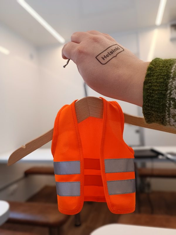 A hand with Helsinki logo holding a small high visibility jacket.