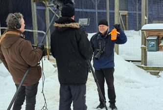 A man holding a small high visibility jacket in front of video camera.